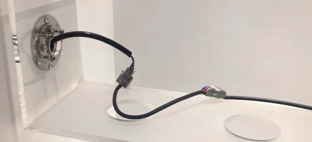 Cable routed through a panel-mounted swivel hinge, with a loose loop and wire connectors inside an enclosure