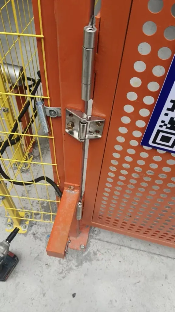 Spring hinge mounted between an orange perforated equipment door and its frame